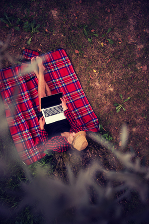 A young freelancer using a laptop computer while working in beautiful nature under the tree top viewの写真素材