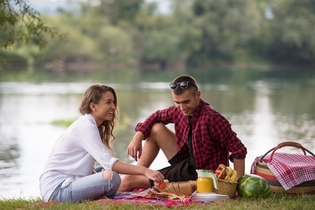 Couple in love enjoying picnic time drink and food in beautiful nature on the river bankの写真素材