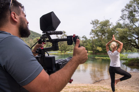 young videographer with gimball video slr rocording while healthy woman doing yoga exercise in the...