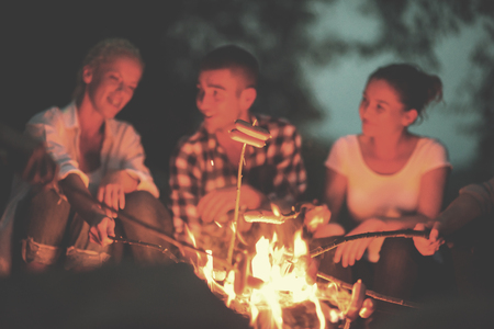 a group of happy young friends relaxing and enjoying  summer evening around campfire on the river bankの写真素材