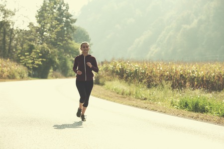 young woman enjoying in a healthy lifestyle while jogging along a country road, exercise and fitness conceptの写真素材