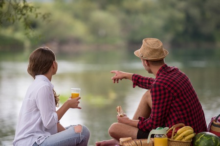 Couple in love enjoying picnic time drink and food in beautiful nature on the river bankの写真素材