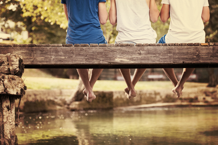 group of  people sitting at wooden bridge over the river with a focus on hanging legsの写真素材
