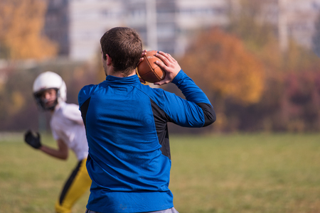 Team coach throwing the ball into the group of young american football players in action during the training at the fieldの写真素材