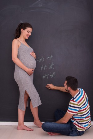 young pregnant couple accounts week of pregnancy and writing them with chalk on blackboardの写真素材