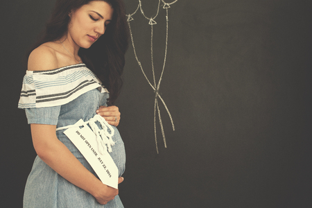 Portrait of happy pregnant woman with hands on belly in front of black chalkboardの写真素材