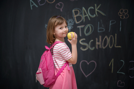 happy child with apple and back to school drawing in background on black chalkboardの写真素材