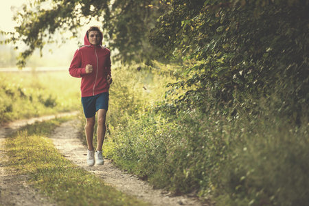 Young man enjoying in a healthy lifestyle while jogging along a country road, exercise and fitness...