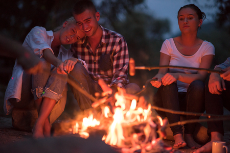 A group of happy young friends relaxing and enjoying  summer evening around campfire on the river bankの写真素材