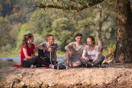 A group of young friends enjoying beautiful sunny day while smoking hookah on the river bankの写真素材