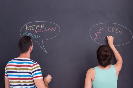 A young pregnant couple thinking about names for their unborn baby and writing them on a black chalkboardの写真素材