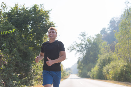 A young man enjoying in a healthy lifestyle while jogging along a country road, exercise and fitness...