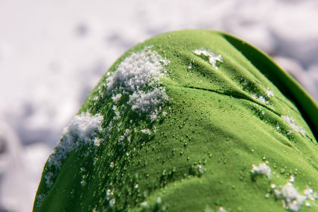 Snow and  water droplets on green waterproof fabric from skiing clothes in winter