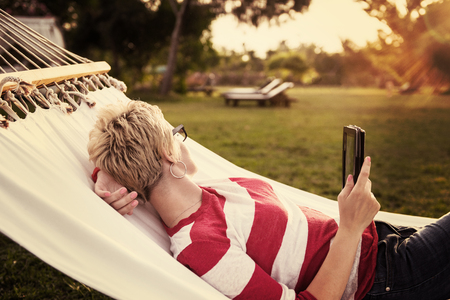 young woman using a tablet computer while relaxing on hammock in a peaceful garden during holidayの写真素材
