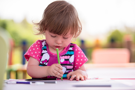 cute little girl cheerfully spending time using pencil crayons while drawing a colorful pictures in the outside playschoolの写真素材