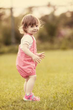 playful cute little girl cheerfully spending time while running in the spacious backyard on the grassの写真素材