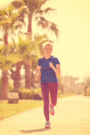 young sporty female runner training for marathon running at beautiful tropical park in the sunny morningの写真素材
