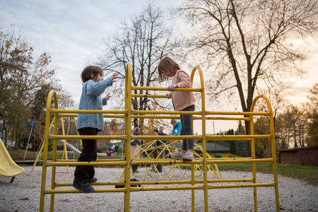 cutte little girl and boy in childrens park having fun and joy while playing in playground on autumn...