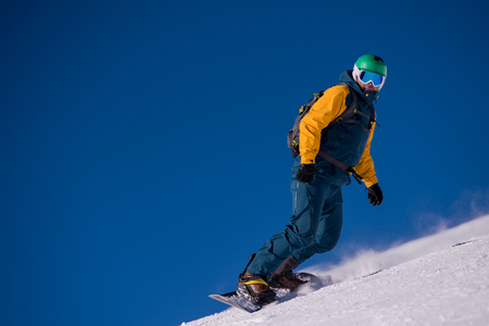 Young freestyle snowboarder running down the slope and ride free style at sunny winter day on Alpine mountains.の写真素材