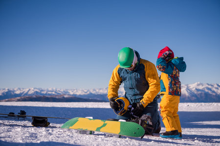 Young happy father preparing his little son for the first time on a snowboard during sunny winter day at beautiful  ski resortの写真素材