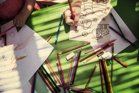 Young mother and her little daughter cheerfully spending time together using pencil crayons while...
