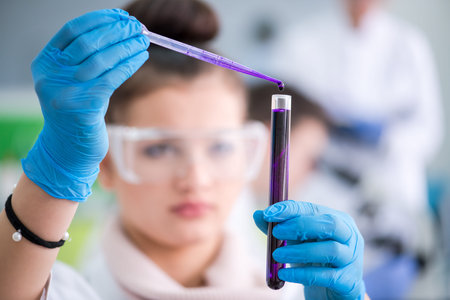 Young female student with protective glasses making chemistry experiment in bright...