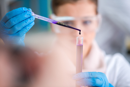 young female student with protective glasses making chemistry experiment in bright laboratory,education and medicine conceptの写真素材