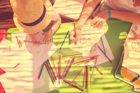 young mother and her little daughter cheerfully spending time together using pencil crayons while drawing a colorful pictures in the outside playschoolの写真素材