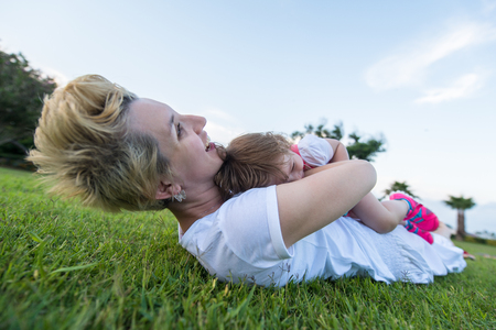 Young Mother and cute little daughter enjoying free time playing outside at backyard on the grass, happy family in nature conceptの写真素材