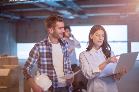 Young team of business people in group, architect and engineer on construction site checking documents and business workflow using laptop computer in new startup officeの写真素材