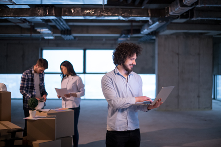 Young male architect on construction site checking documents and business workflow using laptop computer with colleagues in the new startup officeの写真素材