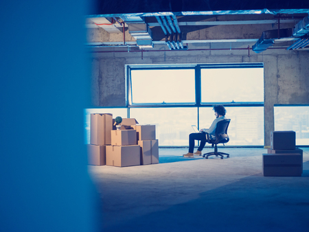 Young male architect on construction site checking documents and business workflow using laptop computer with cardboard boxes around him in new startup officeの写真素材