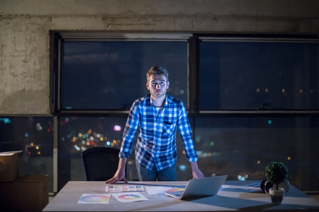 Portrait of young male engineer on construction site checking documents and business workflow using laptop computer in new startup office at nightの写真素材