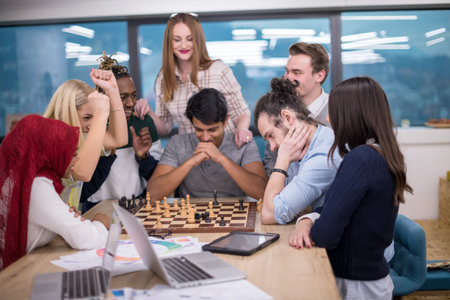 A multiethnic group of business people playing chess while having a break in modern startup office