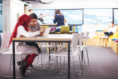 successful black muslim business woman having a meeting with her indian male colleague working on the laptop at modern startup officeの写真素材