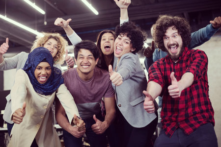 Portrait of young excited multi ethnics business team of software developers standing and looking at camera while celebrating success at modern startup officeの写真素材