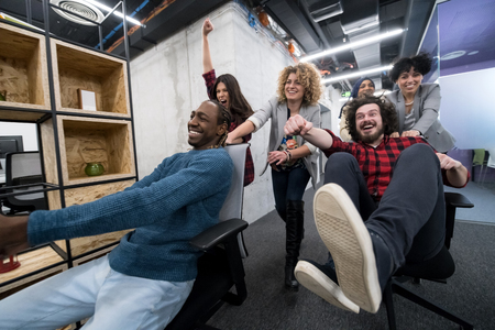 Multiethnics startup business team of software developers having fun while racing on office chairsの写真素材