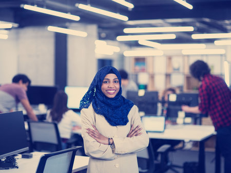 Portrait of young muslim african american female software developer with blue scarf standing at...
