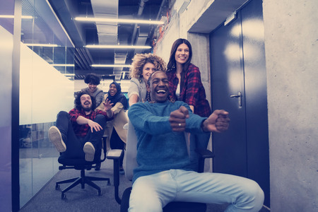 Young multiethnics startup business team of software developers having fun while racing on office chairの写真素材