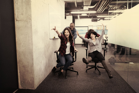 Young multiethnics startup business team of software developers having fun while racing on office chairsの写真素材
