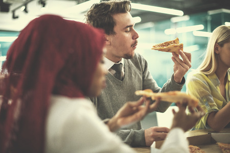 Friendly diverse multiethnic business team eating sharing pizza together in startup officeの写真素材