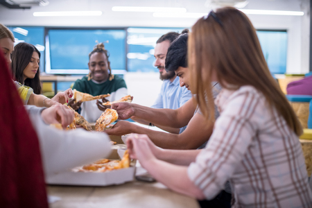 Friendly diverse multiethnic business team eating sharing pizza together in startup officeの写真素材