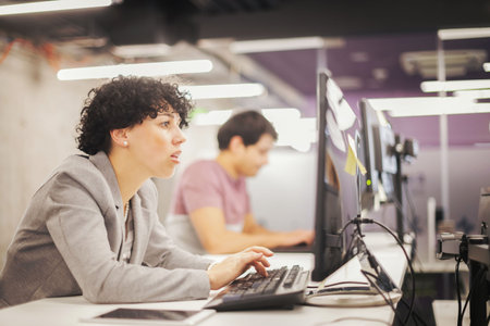 Young female software developer using desktop computer while writing programming code at modern creative startup officeの写真素材