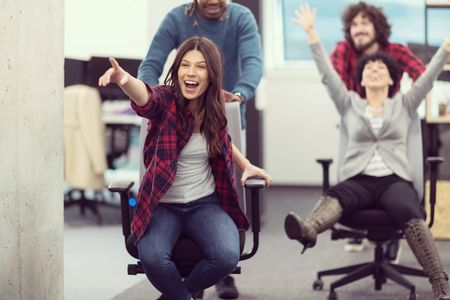 Young multiethnics startup business team of software developers having fun while racing on office chairsの写真素材