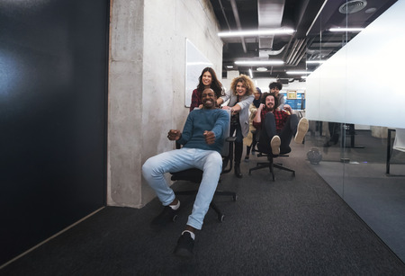 Young multiethnics startup business team of software developers having fun while racing on office chairsの写真素材