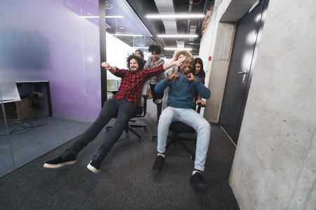 Multiethnic startup business team of software developers having fun while racing on office chairsの写真素材