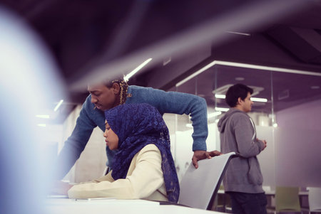 Muslim female software developer working together with her african american male colleague using computer while writing programming code at modern startup officeの写真素材