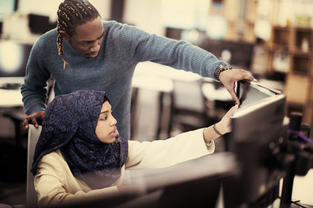 Muslim female software developer working together with her african american male colleague using...