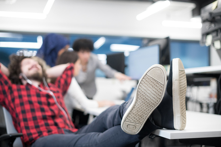 Young software developer resting with legs on desk while his multiethnics business team writing programming codeの写真素材