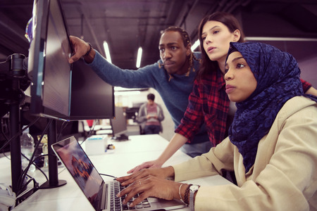 Young multiethnics business team of software developers working together using laptop computer while writing programming code at modern startup officeの写真素材